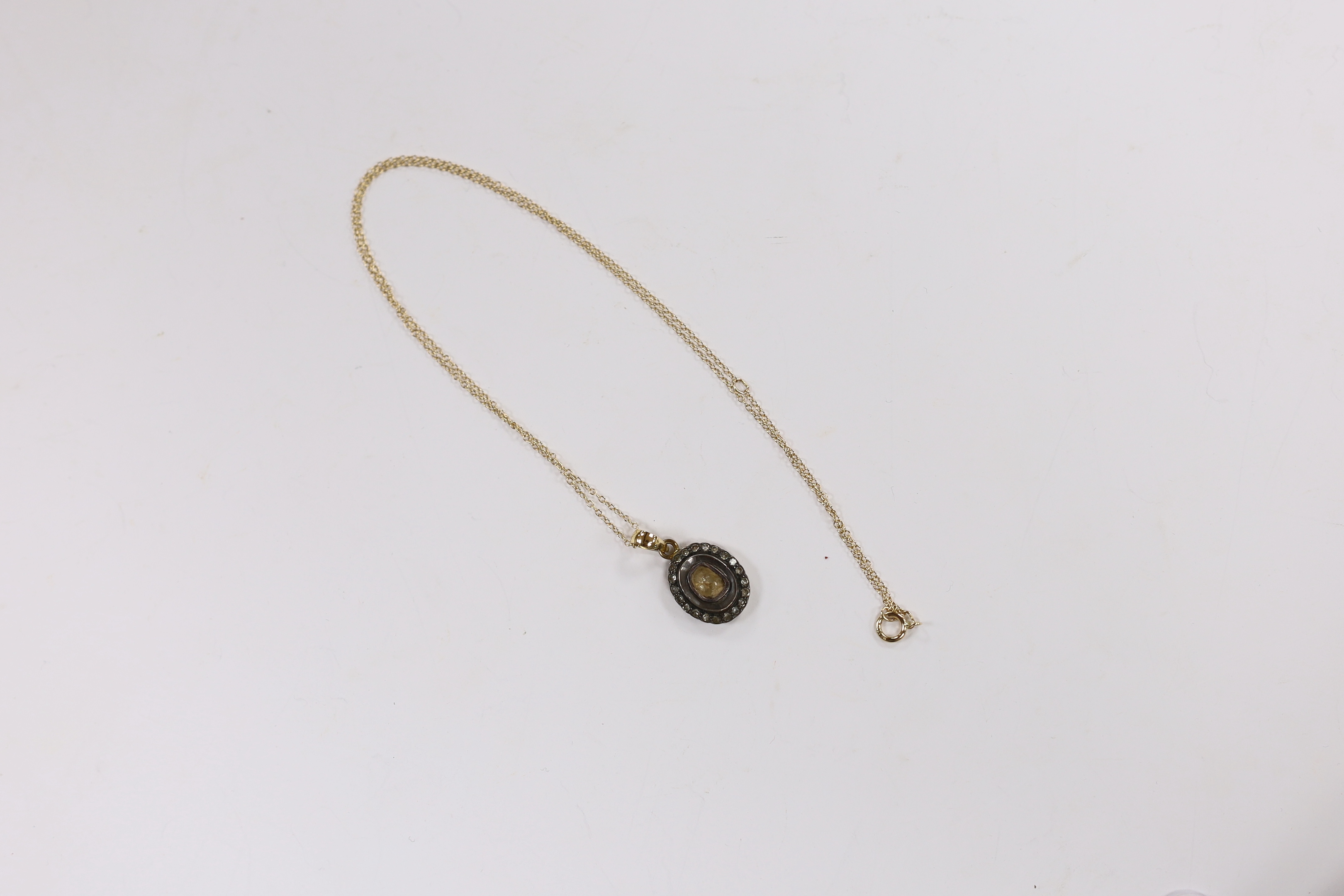 A suite of Indian yellow metal and diamond cluster set suite of jewellery, comprising an oval pendant (overall 22mm), on a 14k chain, 44cm and a pair of matching earrings, 14mm, gross weight 8.2 grams.